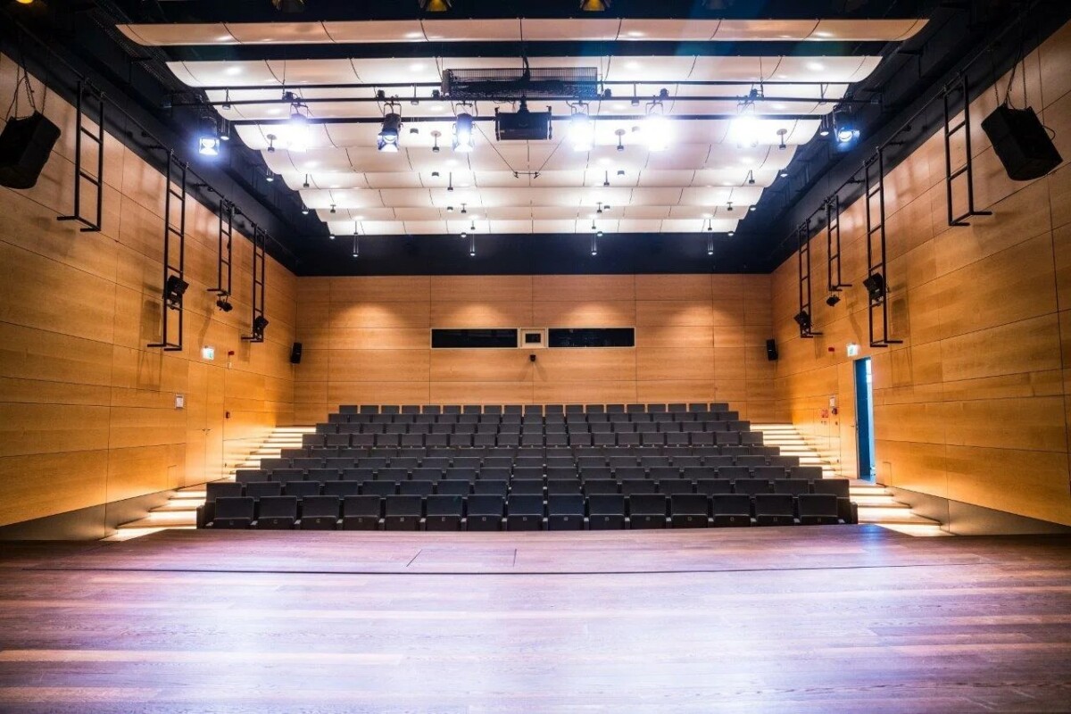 Salle de cinéma vide avec sièges noirs, murs en brique orange et éclairage moderne bleu et blanc